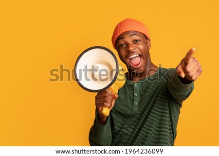 Cheerful Black Guy Shouting In Loudspeaker And Pointing At Camera, Excited African American Man Holding Megaphone, Making Announcement, Standing Isolated Over Yellow Background, Copy Space Royalty-Free Stock Photo #1964236099