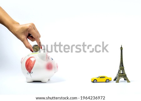 Travel or vacation money saving concept. Hand hold coin, pink piggy bank with car and Eiffel tower isolated on white background. Vacation budget saving by working. Europe Holiday planning concept