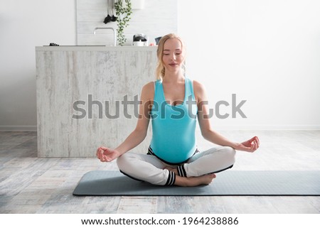 pregnant woman meditates sitting in a lotus position on the floor of the houme
