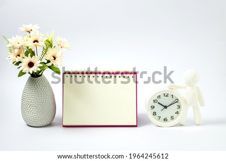 Minimal concept home interior with decor. Mockup with empty note book and white vase. flower blossom in modern pot, isolated on white background. businessman white alarm clock on table wall