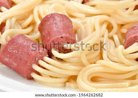 Close-up image of uncooked spaghetti that are used to skewer sliced hot dog  