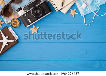 Above photo of camera plane compass map starfish notebook pen sanitizer sunglasses mask and passport with covid-19 test inside isolated on the blue wooden background with empty space