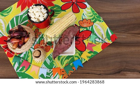 Table with colored cloth, straw hat, pine nuts, paçocas, corn and sweet potatoes, on the table. Typical june foods to celebrate the traditional Brazilian june party.