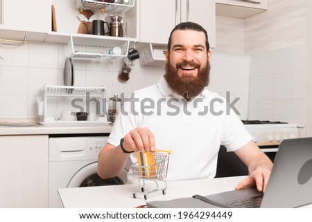Excited because of the possibility to buy online and paying with credit card. Bearded man sitting in a kitchen with his laptop.