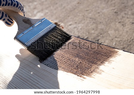 Painting a wooden board outdoors. Coated with protective oil against decay and moisture. paint brush and work gloves