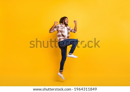 Full length body size photo of man jumping high gesturing like lottery winner laughing isolated on vibrant yellow color background