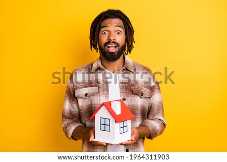 Photo of impressed funny dark skin guy wear checkered shirt holding small house isolated yellow color background