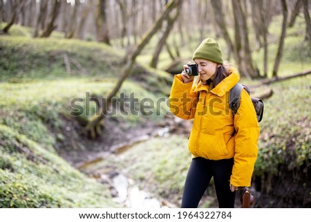 Woman in hiking clothes with backpack takes picture of green spring forest. Enjoys of purity and freshness of nature. Travel alone.