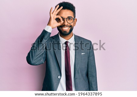 Handsome hispanic business man with beard wearing business suit and tie doing ok gesture with hand smiling, eye looking through fingers with happy face. 