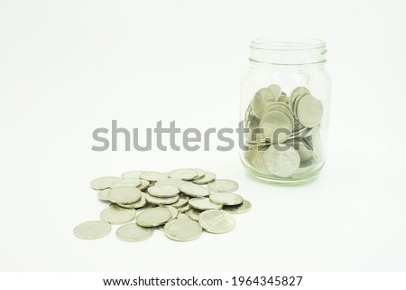 A jar full of coins and coins scattered beside it is isolated on a white background