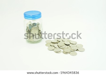 A jar full of coins and coins scattered beside it is isolated on a white background