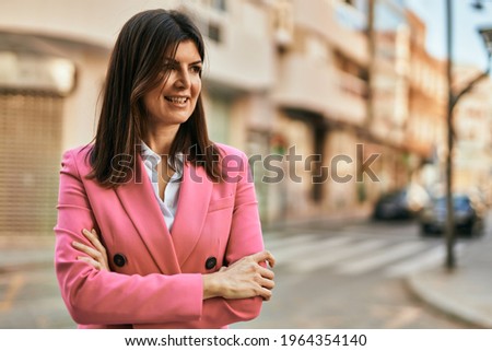 Beautiful hispanic business woman wearing elegant jacket smiling happy at the city with arms closed