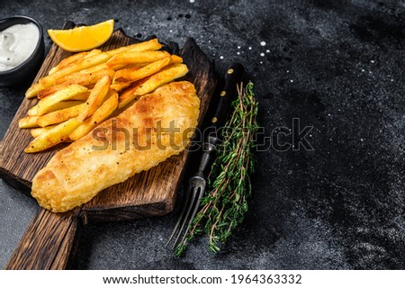 Fish and chips dish with french fries on wooden board. Black background. Top view. Copy space