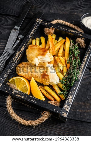 Battered Fish and chips dish with french fries and tartar sauce in a wooden tray. Black wooden background. Top view