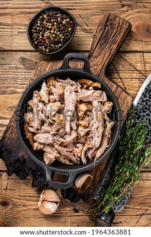 Slow shredded puilled pork meat in a pan with butcher knife. wooden background. Top view
