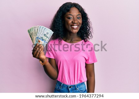 Beautiful african young woman holding dollars looking positive and happy standing and smiling with a confident smile showing teeth 
