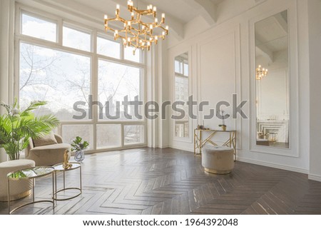 very light and bright interior of luxurious cozy living room with chic soft beige furniture with gold metallic elements, huge window to the floor and wooden parquet Royalty-Free Stock Photo #1964392048