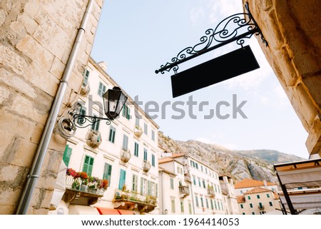 Beautiful black blank sign in a forged frame hangs on the stone wall of the building against the background of the old city on a bright sunny day