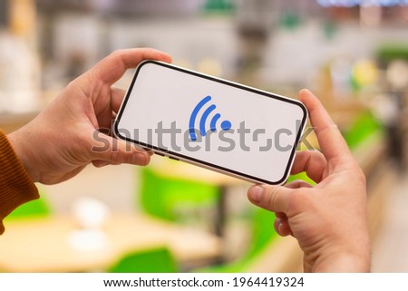 Online payments. Phone display with wi-fi icon against the backdrop of a restaurant. Man holds a smartphone in his hand close-up
