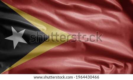 Timorese flag waving in the wind. Close up of East Timor banner blowing, soft and smooth silk. Cloth fabric texture ensign background.