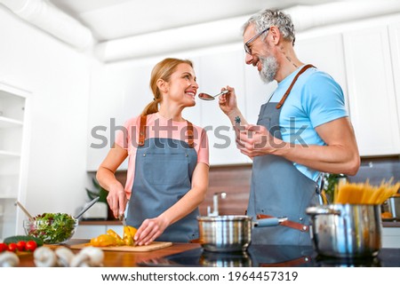 Happy senior couple in aprons are preparing pasta and fresh salad in the kitchen and having a nice time. Vegan, vegetarian, healthy lifestyle concept.