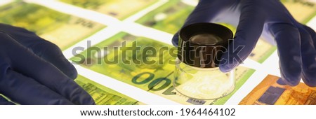 Hands in rubber gloves holding magnifying glass over banknotes closeup