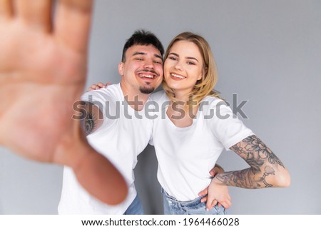 Image of young happy man kissing and hugging beautiful woman while taking selfie photo on gray wall