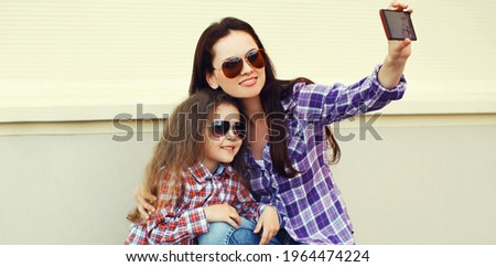 Portrait of happy smiling mother and child taking a selfie picture by smartphone together in the city