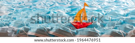 Safety surgical masks arrangement with metaphor of sailing boat on waves on open sea. Summer holiday concept in pandemic era