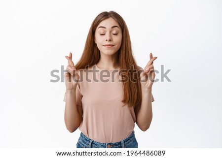 Portrait of hopeful girl student wishing about exam, cross fingers for good luck and close eyes, praying, pleading for dream come true, white background