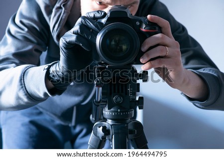 the camera is mounted on a tripod. In the background, the photographer looks at the camera display and presses the shutter button with his index finger.