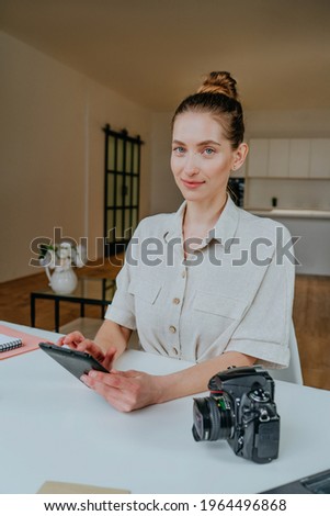 Young beautiful woman with camera using tablet sitting in the living room.