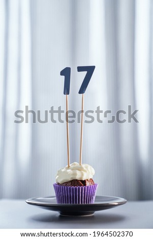 Tasty homemade chocolate creamy cupcake or muffin with topping and number 17 seventeen and bright background. Birthday greeting card concept. High quality vertical image