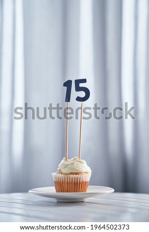 Digital gift card concept. Homemade vanilla anniversary or birthday cupcake with creamy topping and number 15 fifteen with bright background in minimalistic style. High quality vertical image