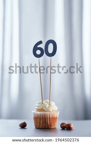Minimalistic anniversary concept. Homemade vanilla birthday cupcake with creamy topping and number 60 sixty on white plate and bright background. High quality vertical image