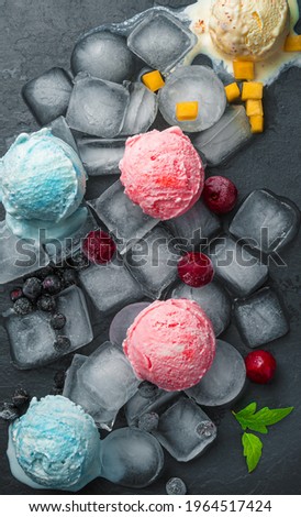 Ice cream balls and berries on ice cubes on a black background. Pitchfork from above, close-up.
