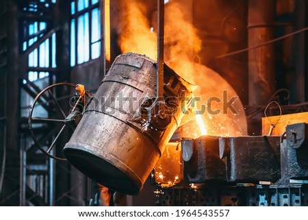 Metal casting process in foundry, liquid metal pouring from container to mold with clubs of steam and sparks, heavy metallurgy industry background Royalty-Free Stock Photo #1964543557