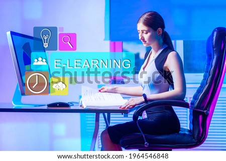 E-learning in business. Businesswoman examines documents next to a computer. She is preparing business training. Electronic learning business management. E-learning symbols in foreground.