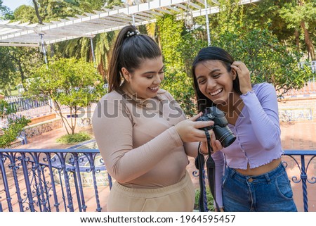 Two friends reviewing the camera photos while laughing. Communication, technology, friendship concept.