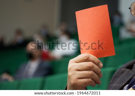 A man - a participant of an election or voting holds a paper red card in his hands. Protest voting, banning or disagreeing with the decision. Close-up. Reportage. No face