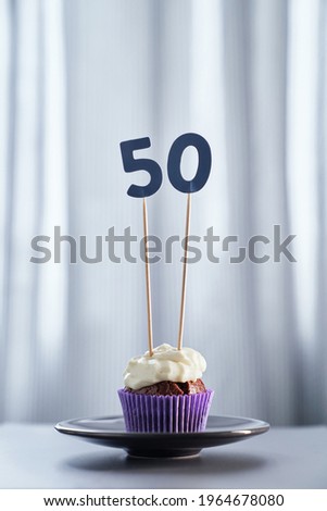 Digital gift card anniversary concept. Tasty homemade chocolate birthday cupcake with white creamy topping and number 50 fifty with bright background in minimalistic style. High quality vertical image