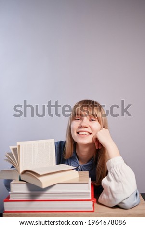 Back to school or homeschooling concept. Blonde female student with stack of books relaxing. Young beautiful caucasian pupil girl with opened book in class with copy space. High quality vertical photo
