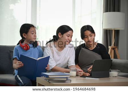 Three young girl sitting on couch and watching cartoon together on digital tablet.