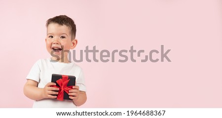 Funny boy in white t-shirt holding black box gift in front, festive banner. Pink studio background. High quality photo