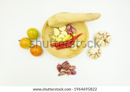 Kitchen seasoning consisting of chilies, garlic, shallots, tomatoes, and pepper on a wooden mortar isolated on a white background.