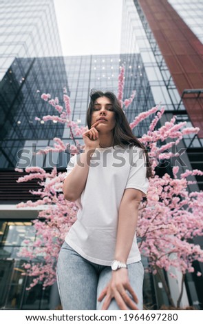 Woman portrait with cherry blossom in the business park. Girl wears white shirt and jeans. Fashion portrait in modern city center