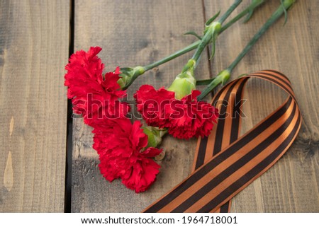 three red carnations with a St. George ribbon on a wooden background. Georgievsk ribbon - Russian symbol of victory and three red carnations. Holiday card for the holiday of May 9. Soft focus