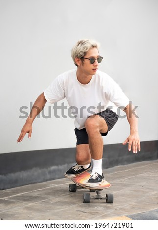 Young asian man riding skateboard on city pavement. Boy in black short pants surf skate board exercising on sidewalk in urban. Skateboarding is trendy outdoor extreme sport through danger. Royalty-Free Stock Photo #1964721901