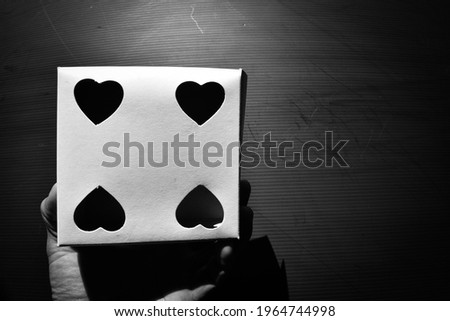 Hand holding a four hearts symbol on white box on the dark background