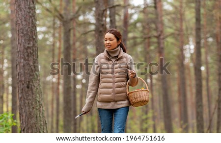 picking season, leisure and people concept - young asian woman with mushrooms in basket walking in autumn forest
